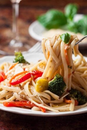 A fork twirling Pasta Primavera with fresh vegetables and a garnish of basil on a wooden table.