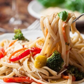 A fork twirling Pasta Primavera with fresh vegetables and a garnish of basil on a wooden table.