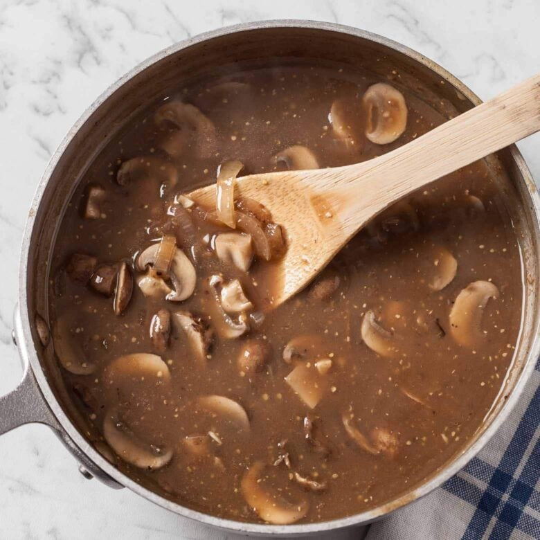 Mushroom gravy for salisbury steak in a saucepan with a wooden spoon.