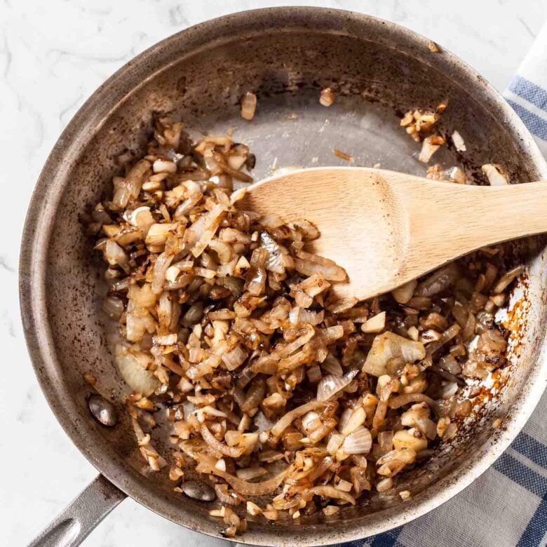 Sautéed onions and garlic in a pan with a wooden spatula.