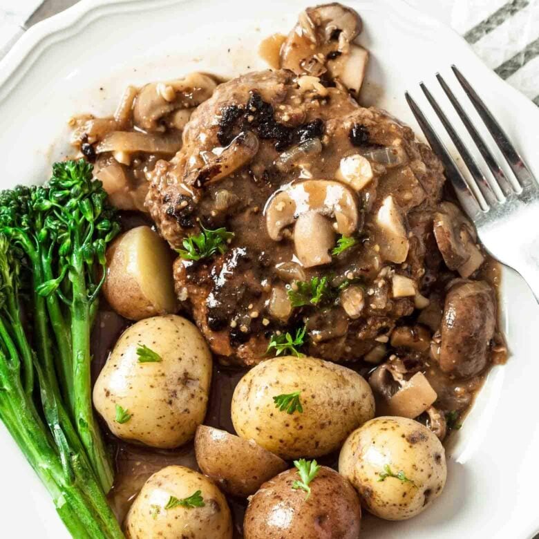 Closeup shot of a plate of salisbury steak with mushroom sauce, baby potatoes, and broccolini.