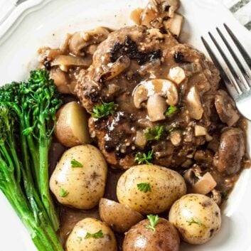 Plate of salisbury steak with mushroom gravy, baby potatoes, and broccolini.