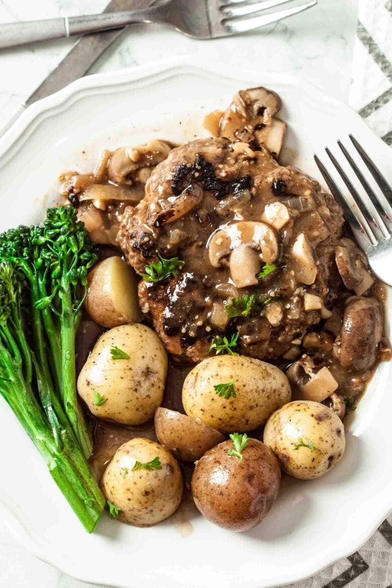 Plate of salisbury steak with mushroom gravy, baby potatoes, and broccolini.