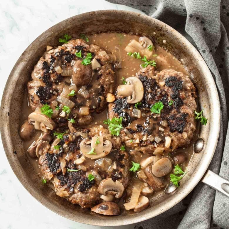 A skillet containing salisbury steak with mushroom gravy and garnished with parsley.