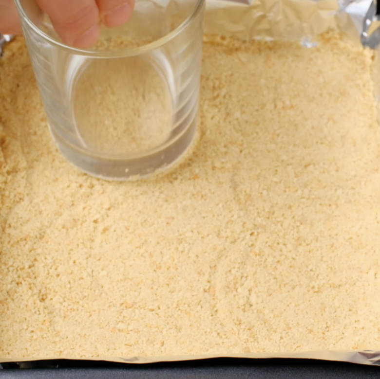 Graham cracker crumb mixture being pressed firmly in a pan.