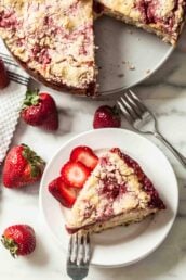 A slice of strawberry crumb cake on a plate with fresh strawberries around it.