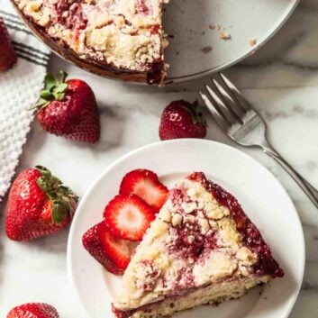 A slice of strawberry crumb cake on a plate with fresh strawberries around it.