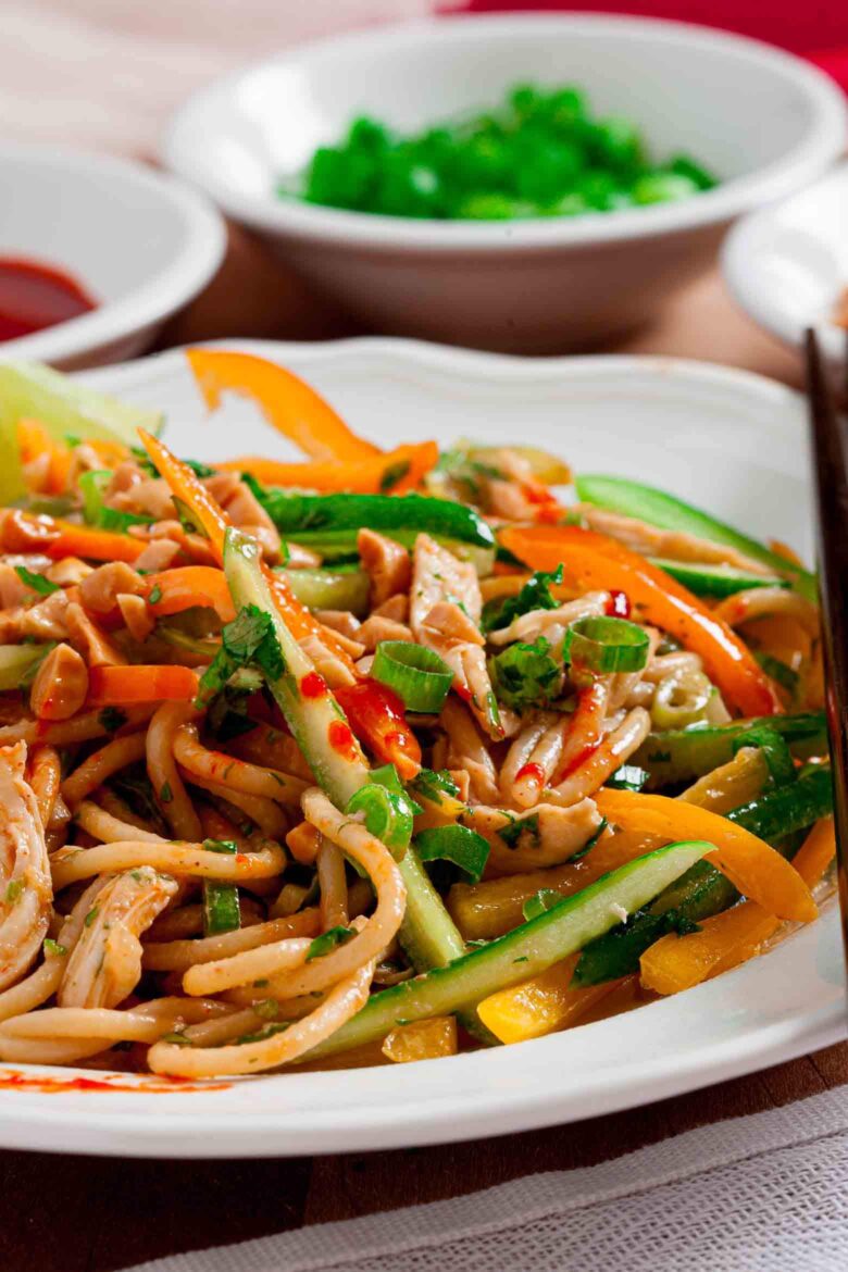 A close-up of a plate of Thai peanut noodles with shredded vegetables.