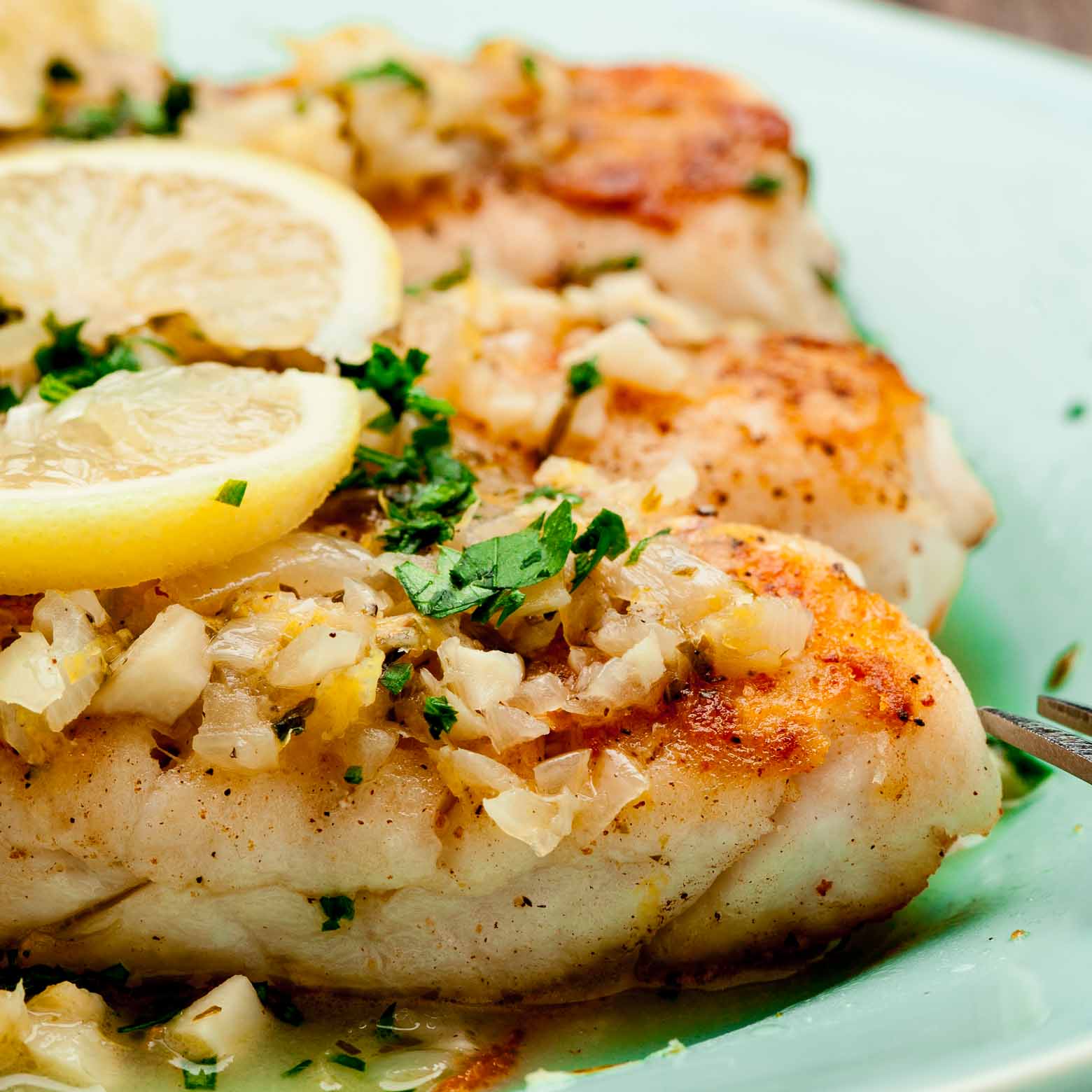 white fish with lemon butter sauce on a plate.