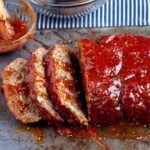 Sliced meatloaf with a glazed topping on a cooking tray.