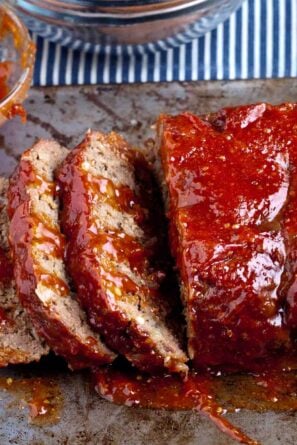 Sliced meatloaf with a glazed topping on a cooking tray.