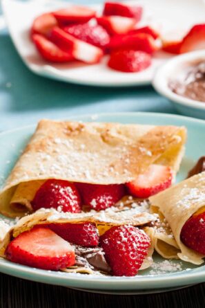 A closeup shot of folded crepe filled with strawberries and Nutella, dusted with powdered sugar.