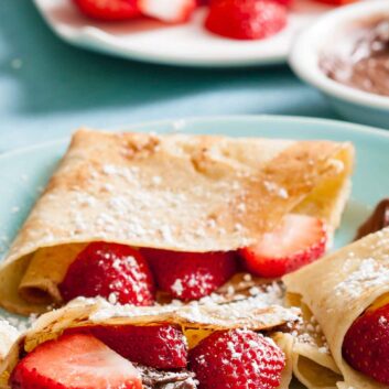A closeup shot of folded crepe filled with strawberries and Nutella, dusted with powdered sugar.