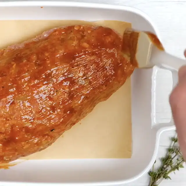 Meatloaf being glazed with sauce before baking.
