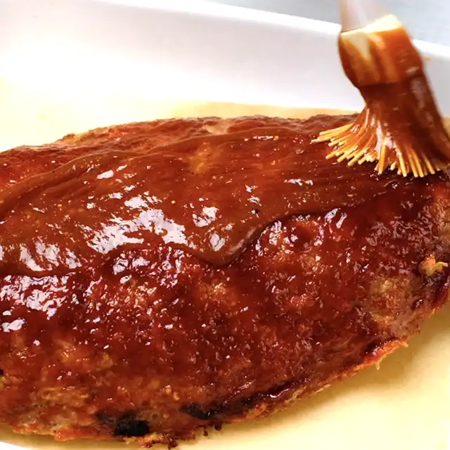 Sauce being brushed over half-baked meatloaf.