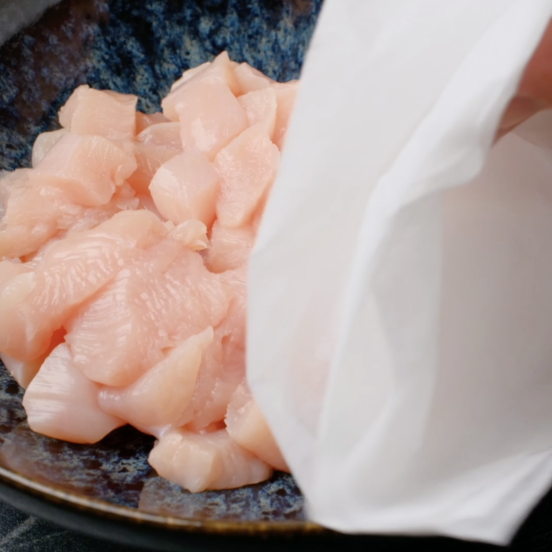 Raw chicken cubes being dried with paper towels.