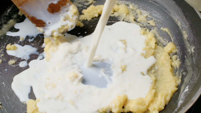 Milk being added to a pot with roux.