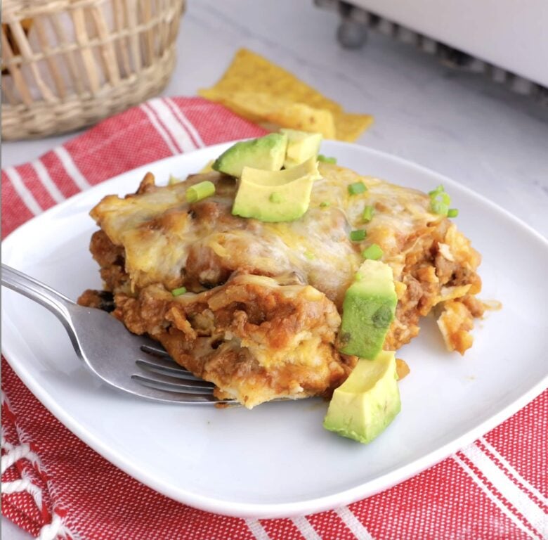 easy enchilada casserole slice on a plate with avocado on top.