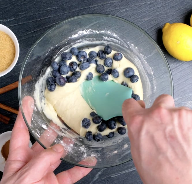Fresh blueberries being folded into muffin batter.
