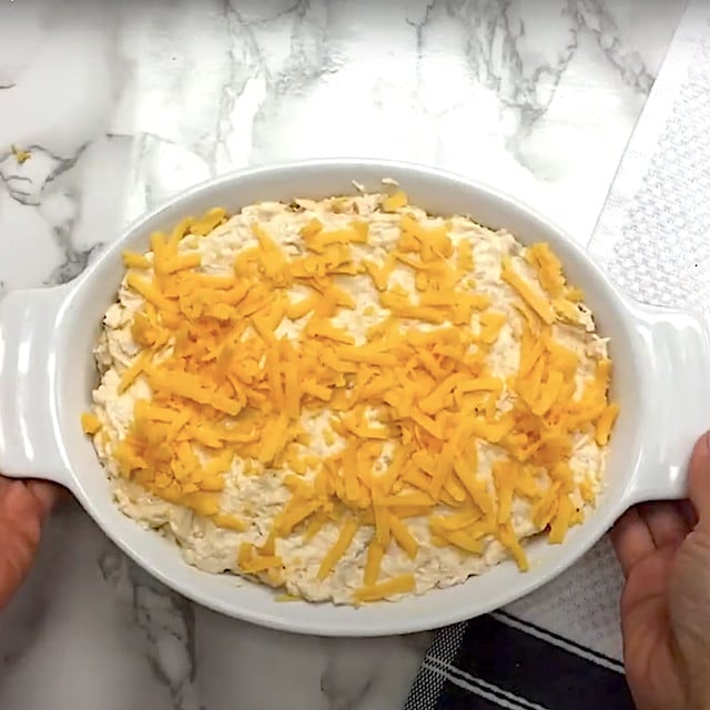 An oval baking dish with buffalo chicken dip topped with cheese, ready to be baked.