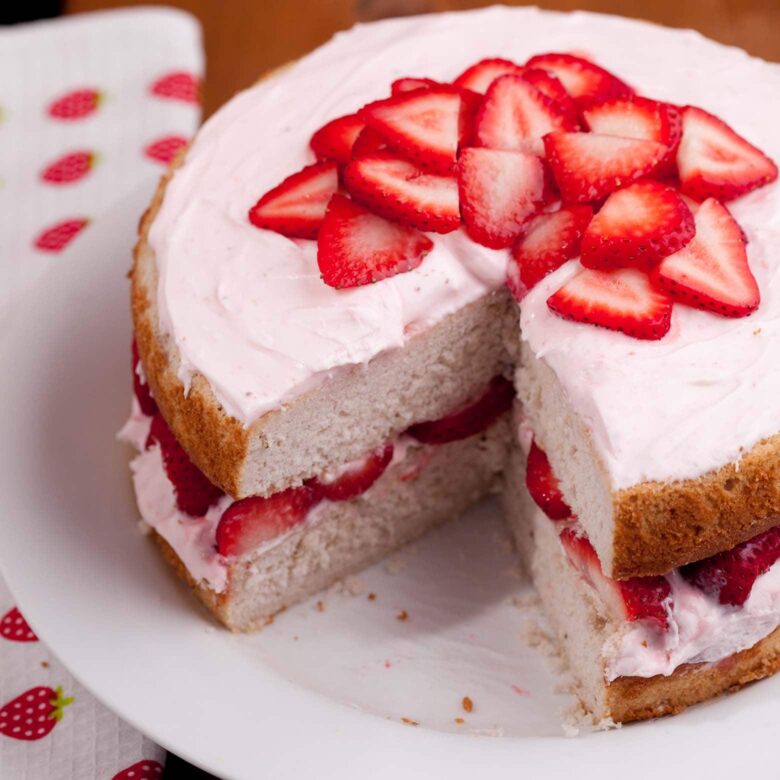 A sliced fresh strawberry cake on a white plate, topped with fresh strawberry slices.