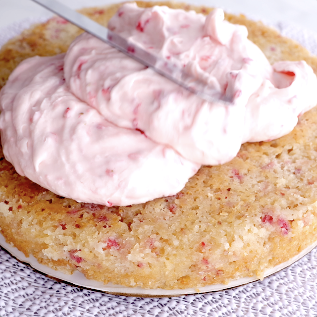 Strawberry frosting being spread on fresh strawberry cake.