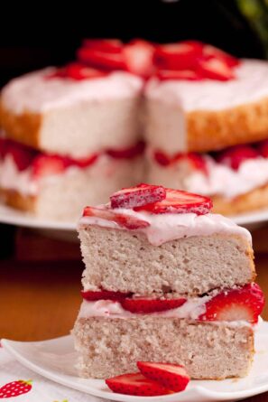Close-up of a slice of strawberry cake on a plate, topped with fresh strawberries and cream.