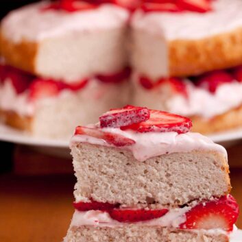 Close-up of a slice of strawberry cake on a plate, topped with fresh strawberries and cream.