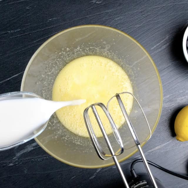 Milk being added to butter, sugar, lemon juice and egg mixture to make lemon blueberry bread.