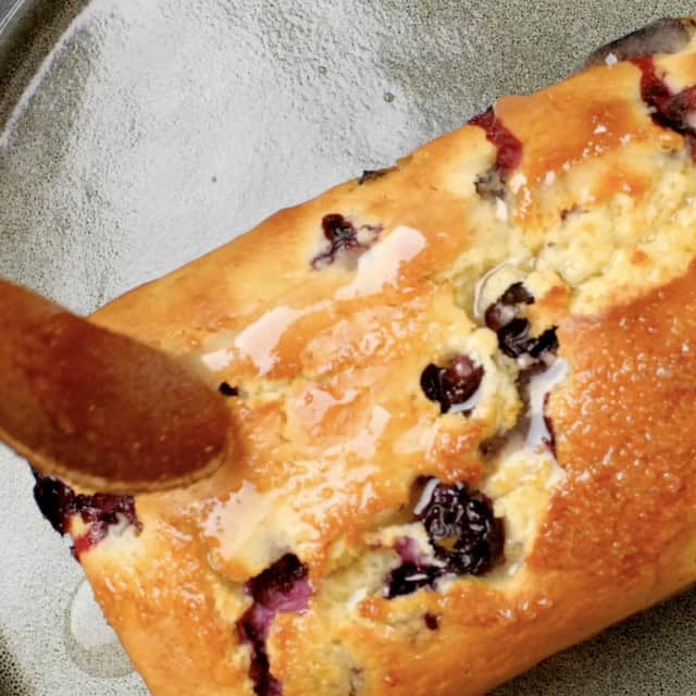 Lemon glaze being poured on top of lemon blueberry bread.