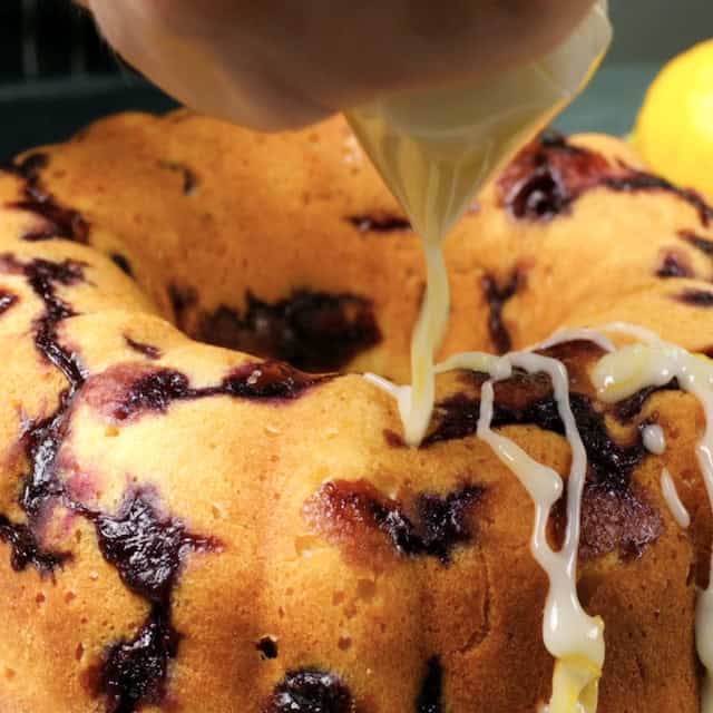 Glaze being poured over cooled freshly baked lemon blueberry bundt cake.