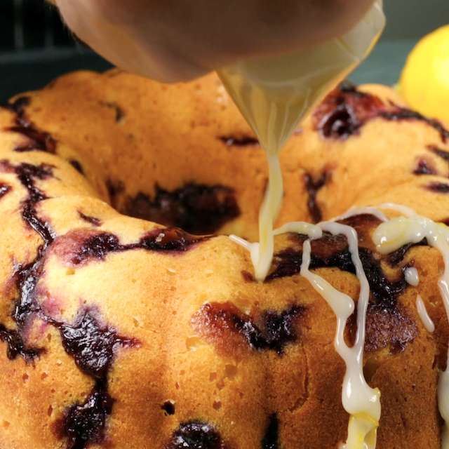 Glaze being poured over cooled freshly baked lemon blueberry bundt cake.