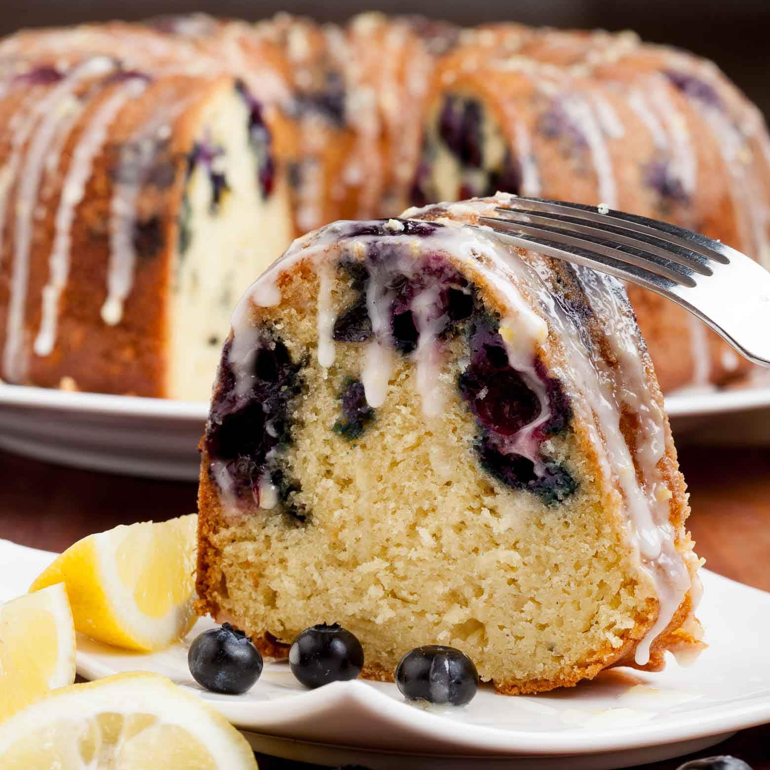 A slice of blueberry lemon bundt cake with icing on a plate, garnished with lemon slices and blueberries.