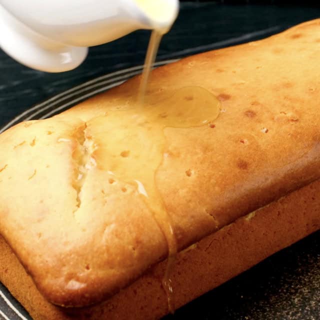 Lemon syrup being poured into lemon olive oil cake with holes poked into it.