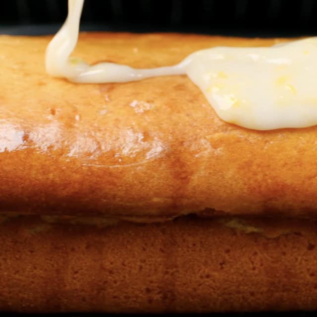 Homemade lemon glaze being poured over lemon olive oil cake.
