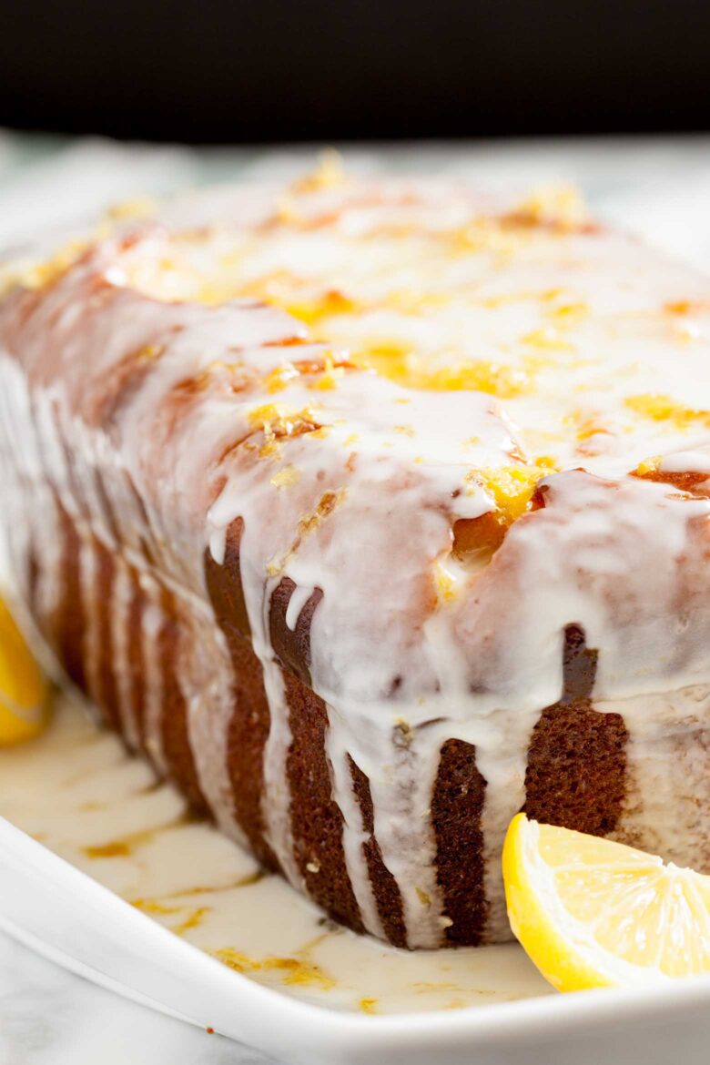 A glazed lemon olive oil cake on a white plate, topped with icing and garnished with lemon slices.