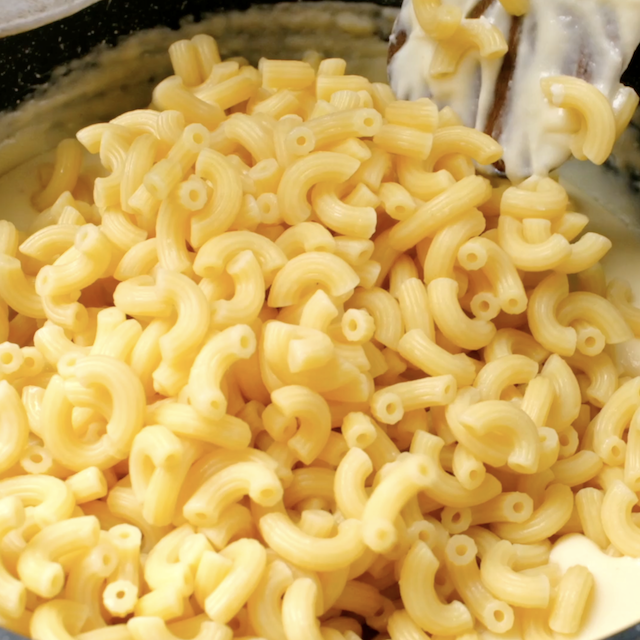 Boiled macaroni being mixed with cheese sauce.