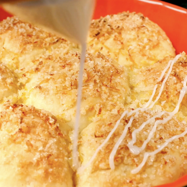 Baked easy lemon rolls being drizzled with glaze.