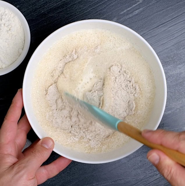 Whole wheat waffle batter being mixed in a large mixing bowl with a spatula.