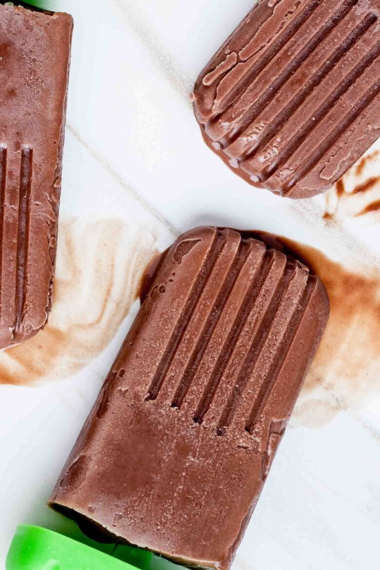 Three chocolate popsicles placed on a white surface with visible melting.
