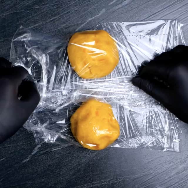 Two cheese cracker dough balls being wrapped in plastic.