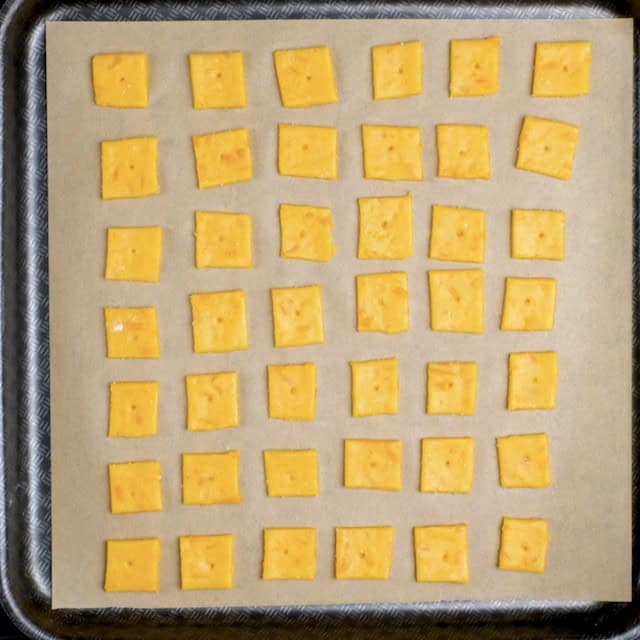 Cheese cracker squares on a lined baking sheet, ready to be baked.