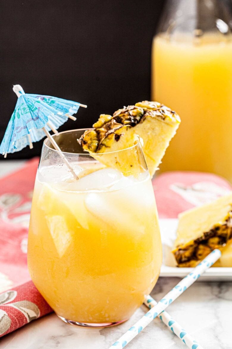A glass of Hawaiian Mai Tai with ice, garnished with a pineapple slice and a blue umbrella.