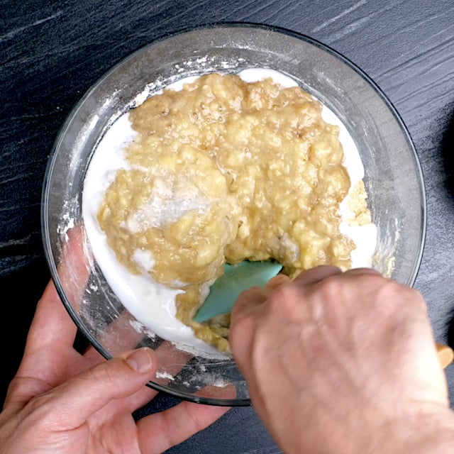 Mashed bananas and yogurt being folded into bread batter.