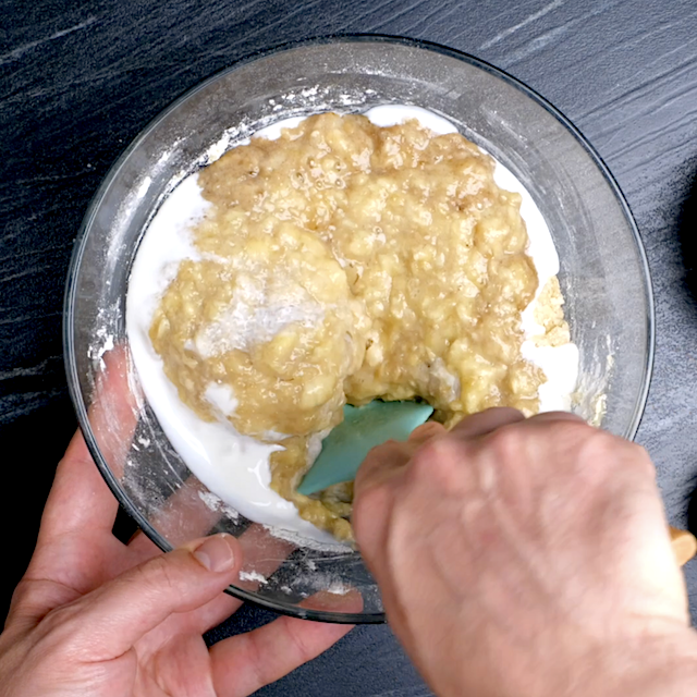 Mashed bananas and yogurt being folded into bread batter.