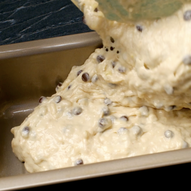 Batter with chocolate chips being poured into a rectangular metal baking pan.