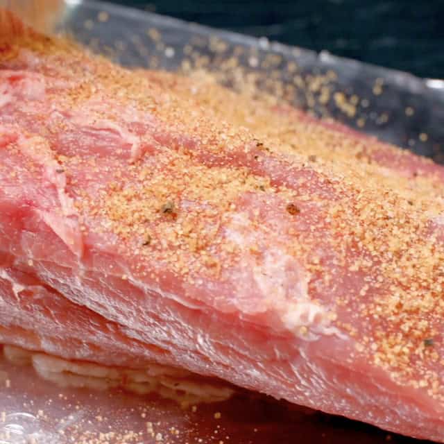 Dry rub being sprinkled generously on pork shoulder to make slow cooker BBQ pulled pork.