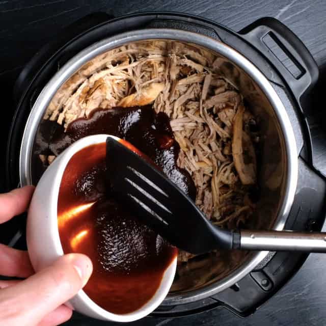 BBQ sauce being added to shredded pork in a slow cooker.