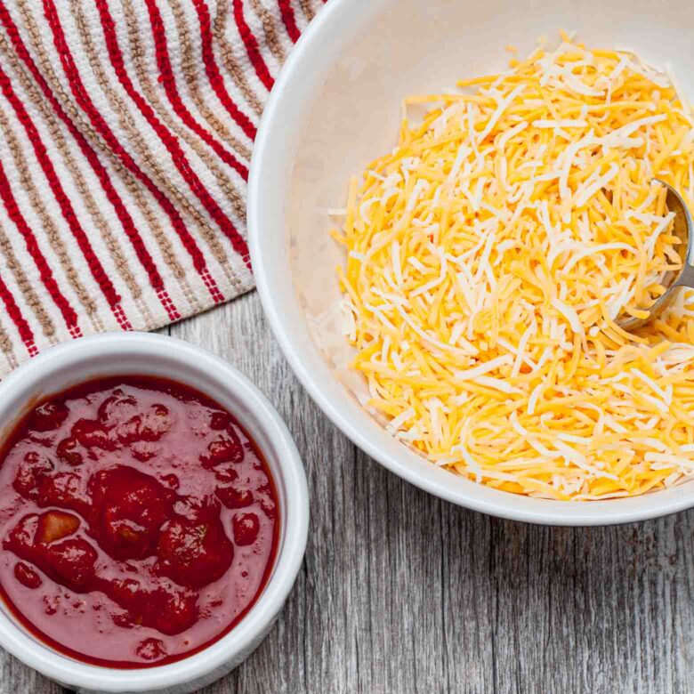A white bowl filled with shredded yellow and white cheese, accompanied by a small white bowl containing salsa.