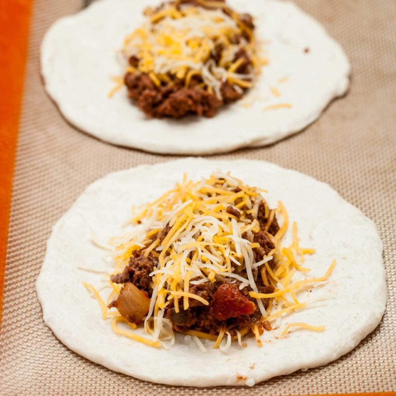 Two uncooked tortilla topped with cooked taco mixture, ready to be baked.